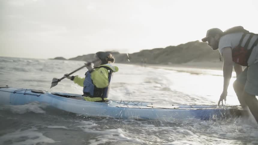 Man pushes a woman in a kayak and she paddles the water