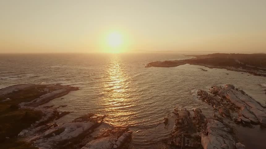 The sun is slowly setting over the rocky shore