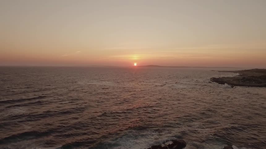 The sun is setting behind the rough waters of this shore