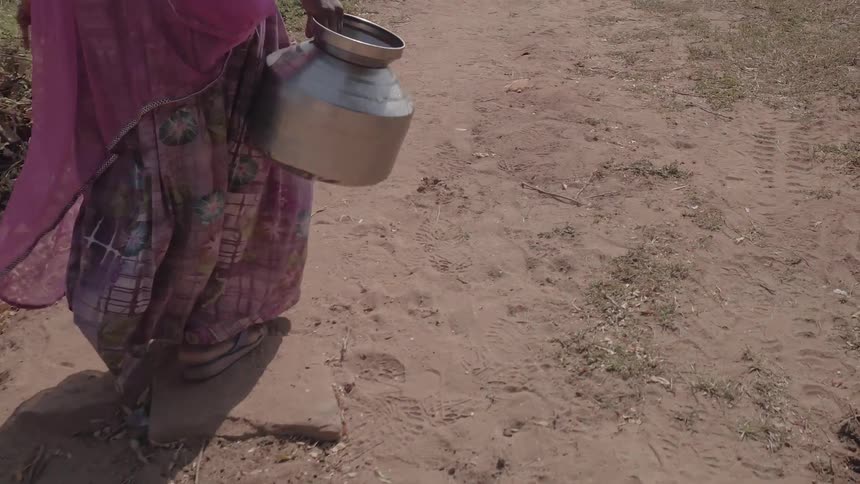 A woman carries a metal jug outside