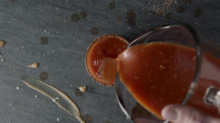 A man is pouring a red liquid into a glass with ice