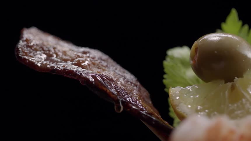Olives and lemon are next to a dripping piece of bacon