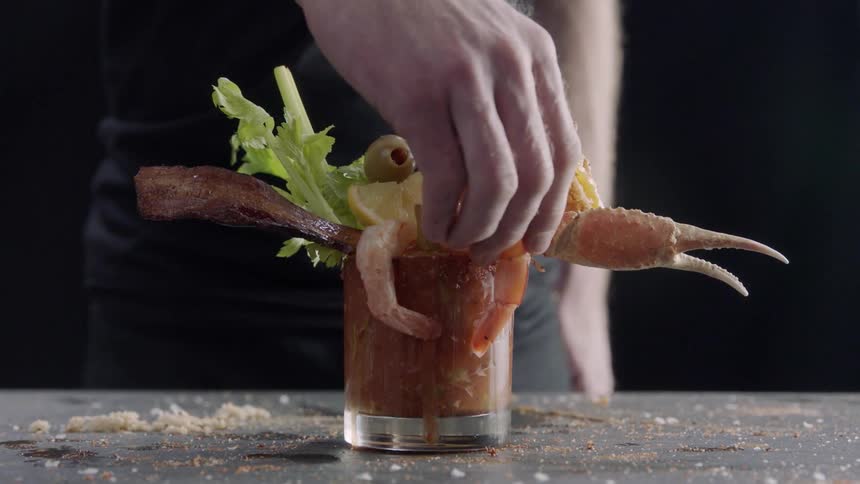 A bloody mary cocktail has bacon, celery and shrimp sticking out of the glass