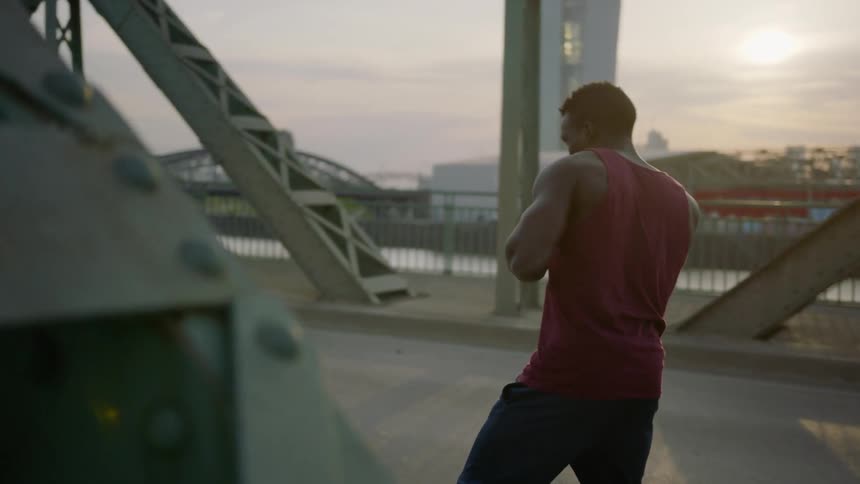 A boxer is shadow boxing on a bridge at dusk