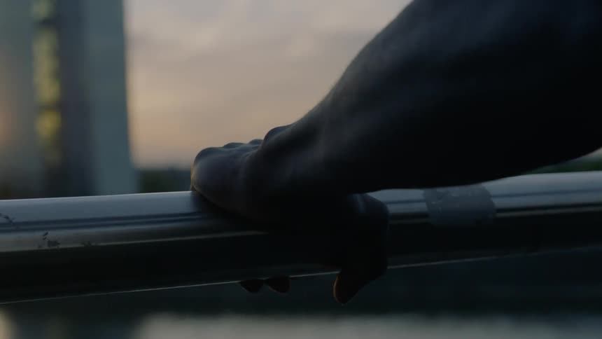 A man leans with his hands on a rooftop railing at sunset