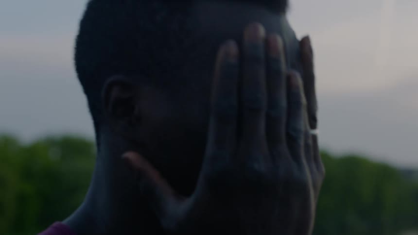 A man is standing outside at dusk rubbing his head and face with his hands