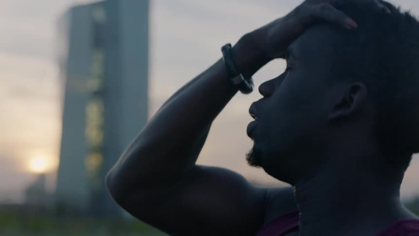 A man standing outside at dusk is rubbing his head and arching it backwards