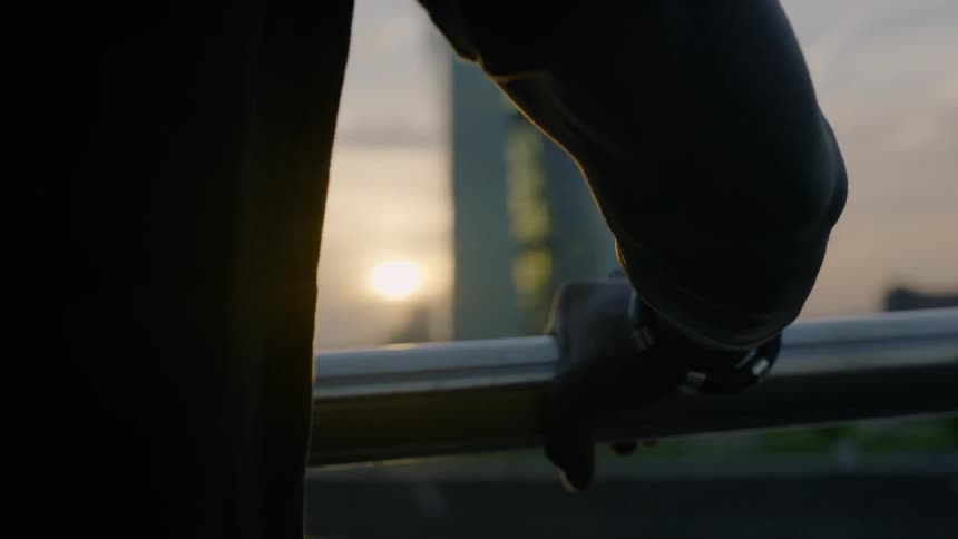 Man holds onto a handrail outside at sunset