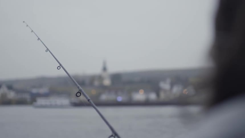 A man is fishing off of a pier next to a big city