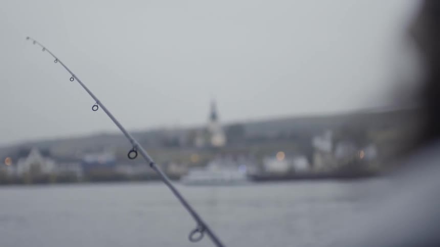 A fisherman reels in his line as a ferry boat passes