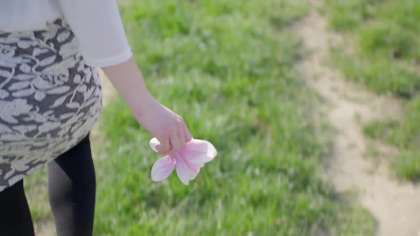 Woman wearing a skirt running while carrying some flower petals in a grassy area