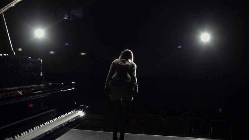 Woman bows on stage next to a piano