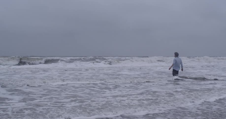A man wades into ocean waves and falls to his knees