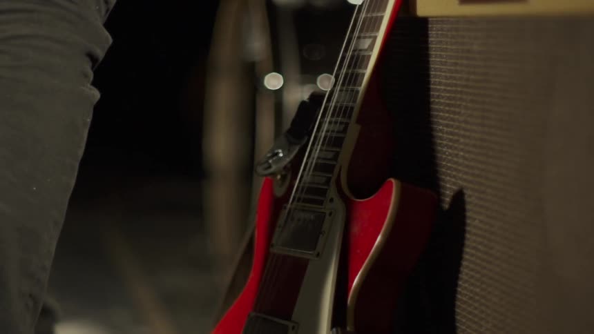 A guitarist places his guitar against an amplifier