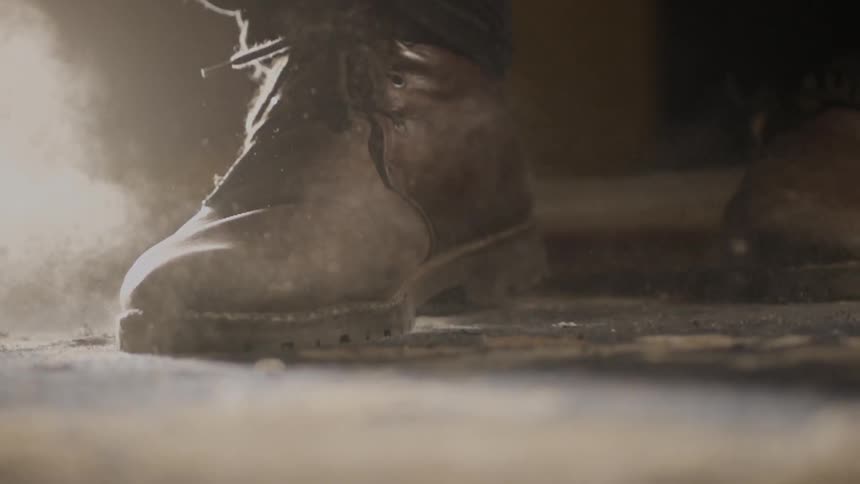 A boot stomps on the ground and dust flies around