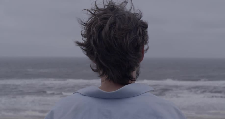 A man is standing looking out at the waves on a stormy day