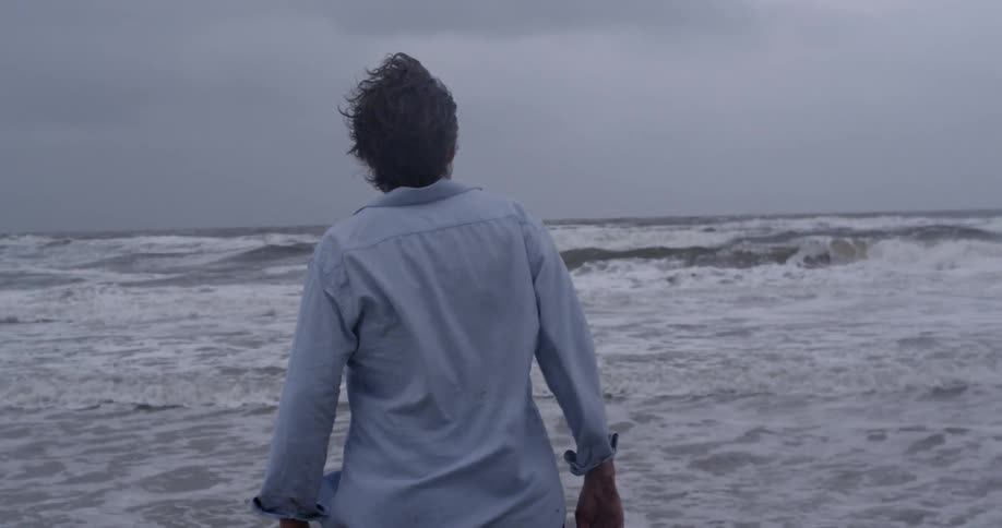 Man wearing a dress shirt walks into the ocean surf