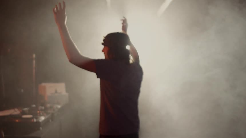 A dj walks onto a smoky stage
