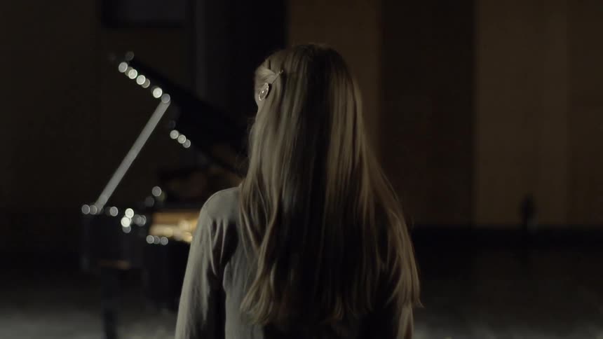 A blonde woman walks on a stage with a piano