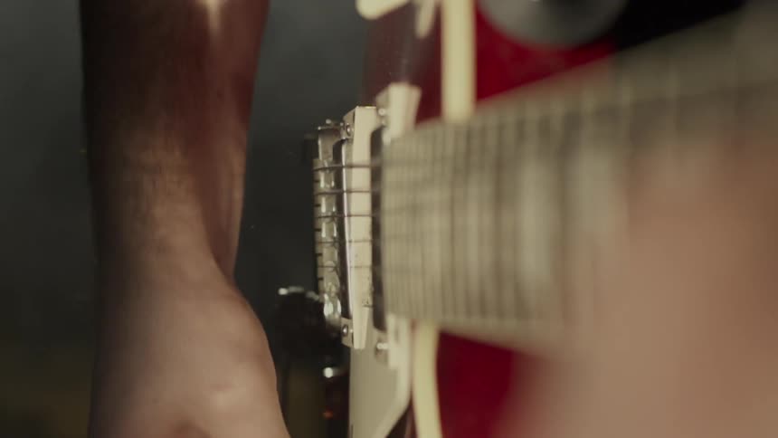 A person is striking the strings of a red electric guitar
