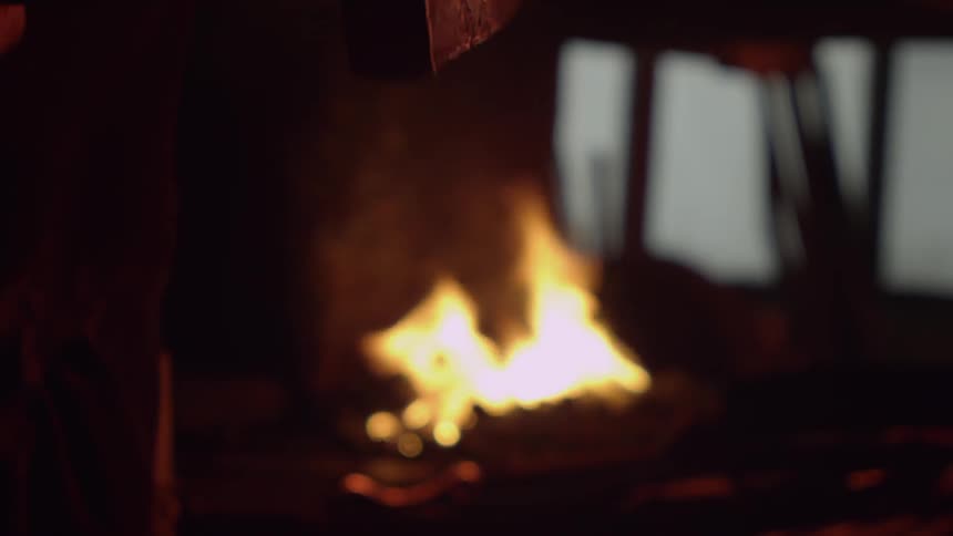 A person turns a hammer by a fire