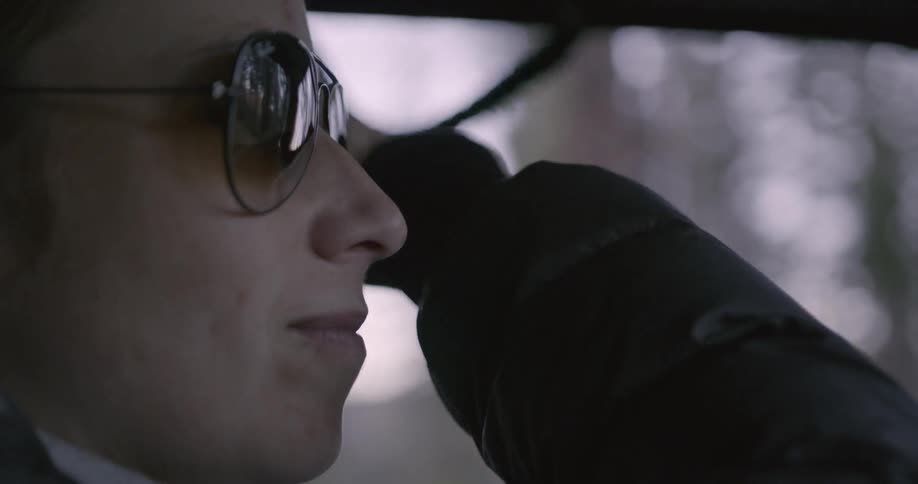 Person putting on sunglasses and adjusting their hair while driving a vehicle