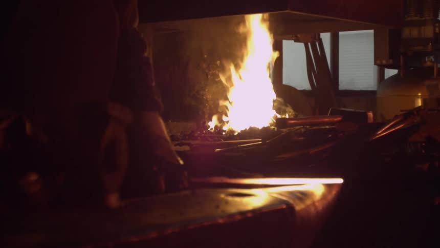 Man heating metal on a fire then hammering it