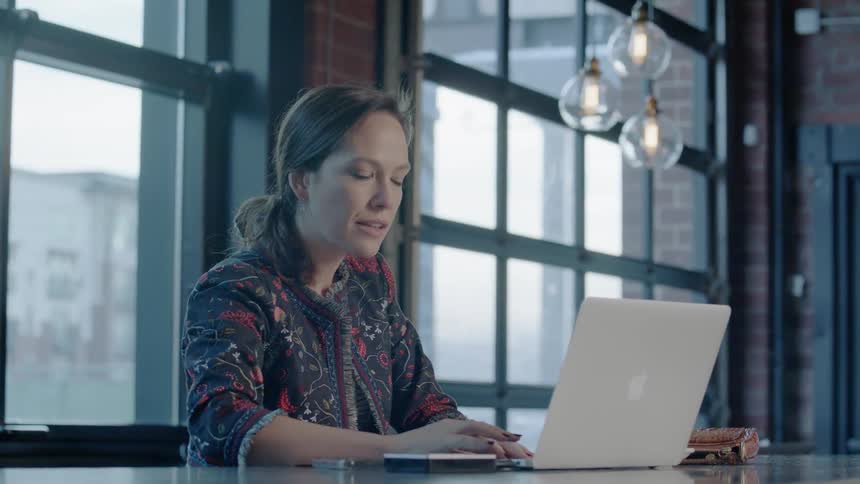 A woman sitting in a bar is opening up a laptop and looking at it