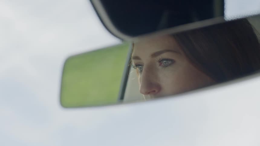 A woman's face can be seen from the rearview mirror