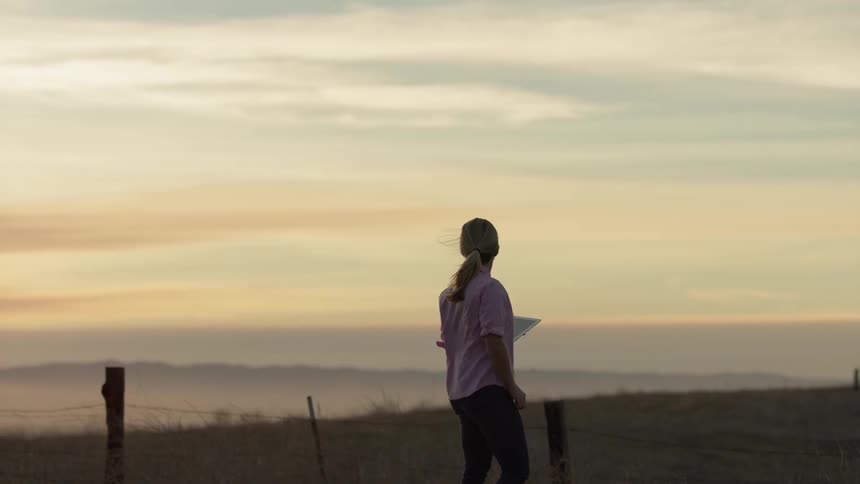 A woman with an ipad is looking at the sunset