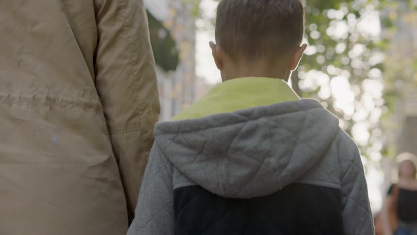 Woman and young boy hold hands while walking on a city sidewalk