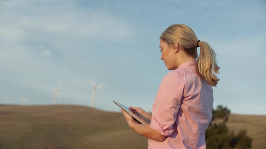Woman stands near wind turbines with a tablet