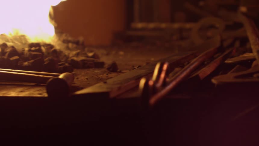 A table full of iron tools with a fire burning beside the pile