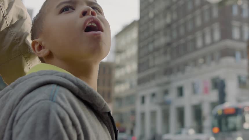 A child with their parent looks up in amazement at the tall buildings