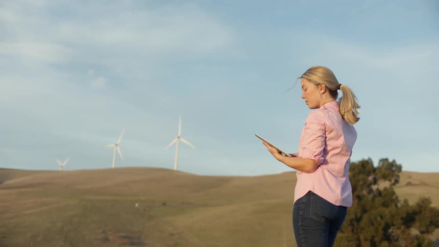 Woman standing with a tablet outdoors with wind turbines turning in a field