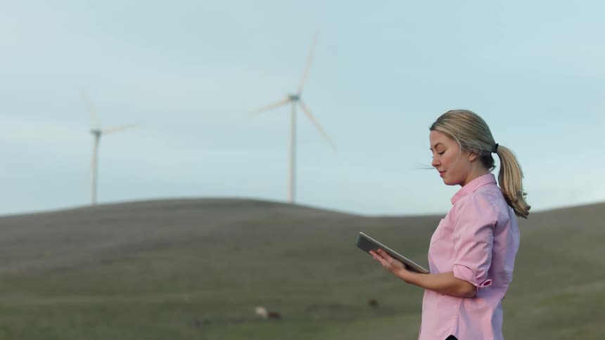 Woman stands near wind turbines with a tablet