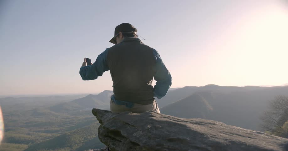 Someone is sitting on the edge of a cliff looking at their phone