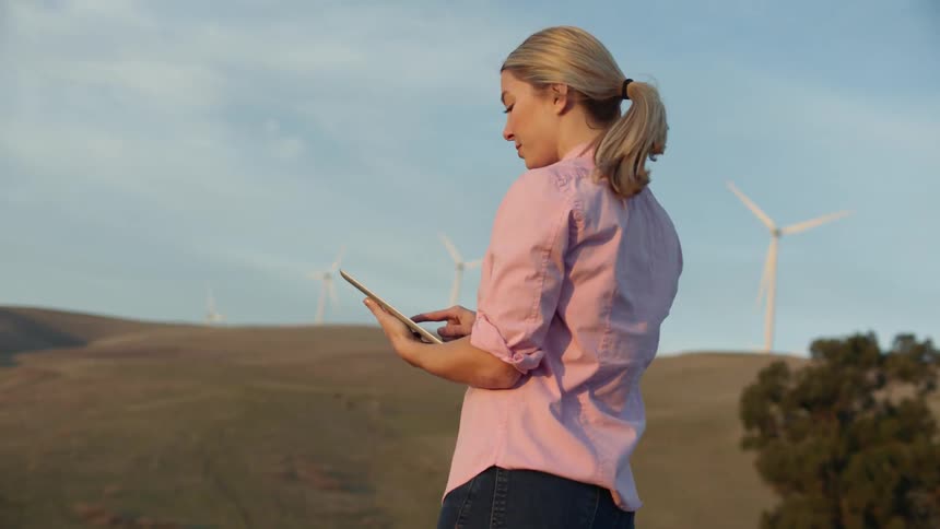 Woman stands near wind turbines with a tablet