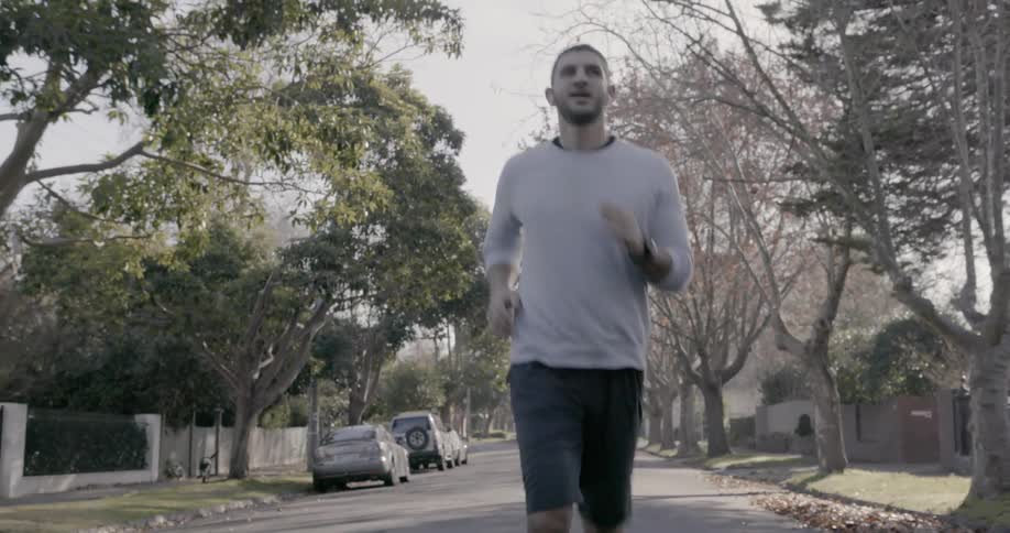 A man is jogging in the middle of a street in a neighborhood during the day