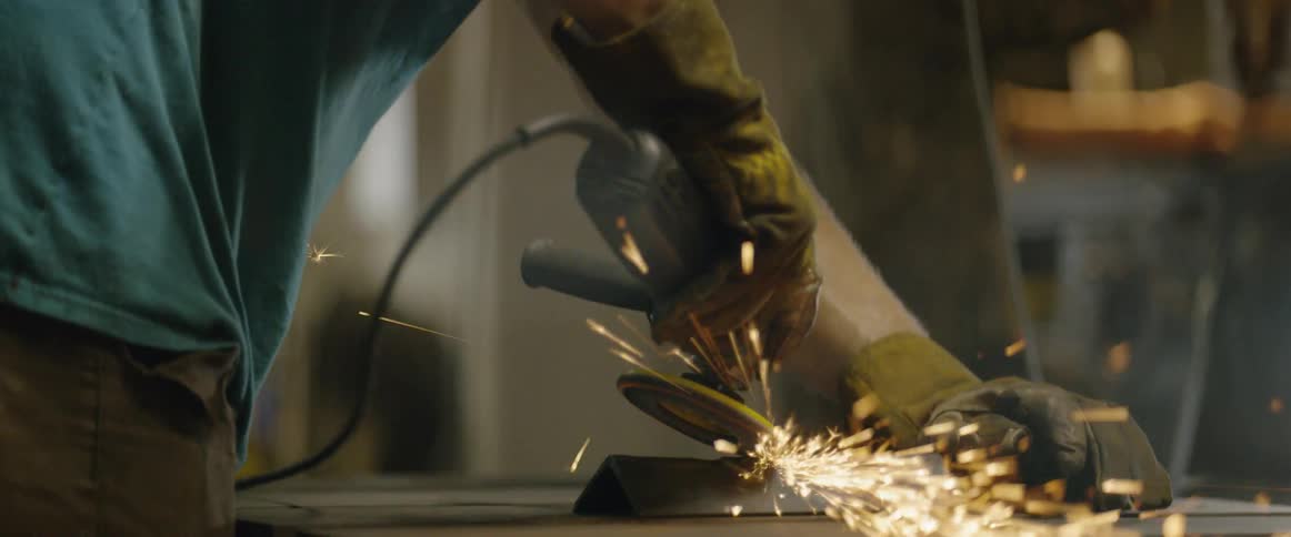 A man uses a grinder on a piece of steel