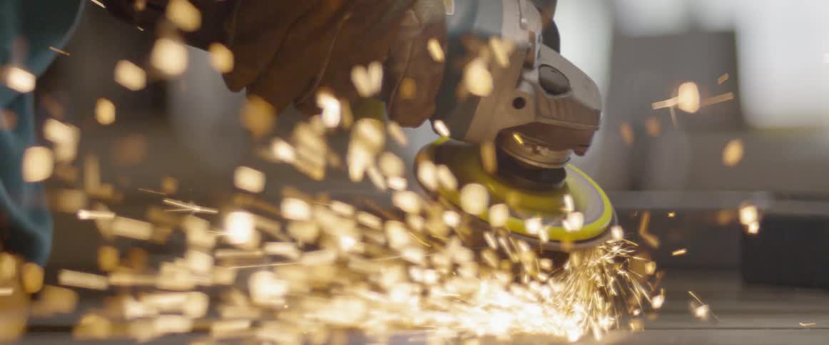 Sparks fly from a grinder as it is used to sand a steel beam