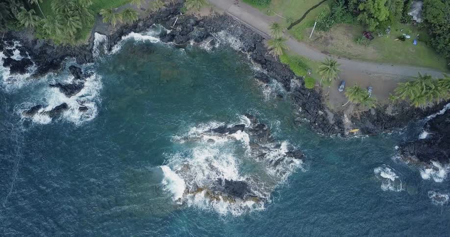 Waves crash over rocks on a tropical shore during the day