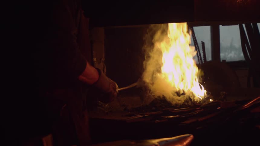 A man heats up a metal tool in a fire