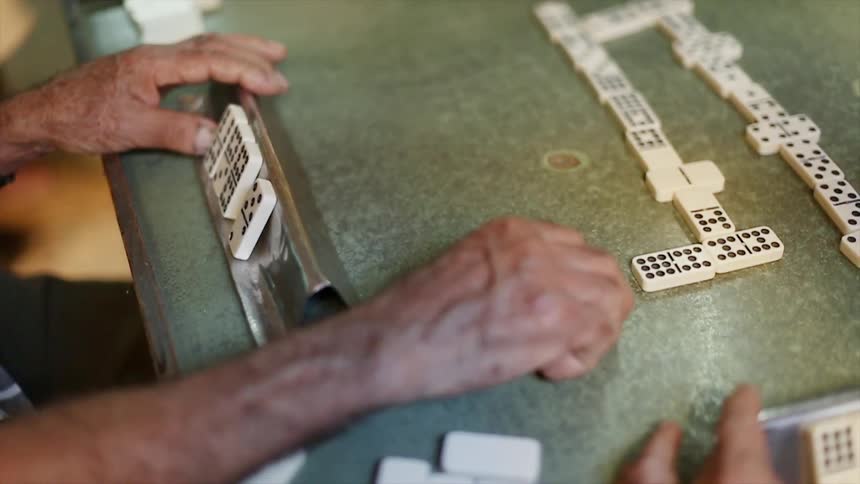 Men sit at a table and play dominoes