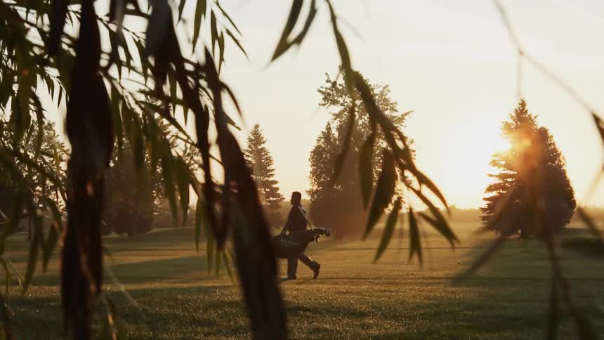 A golfer is walking onto the golf course at sunrise