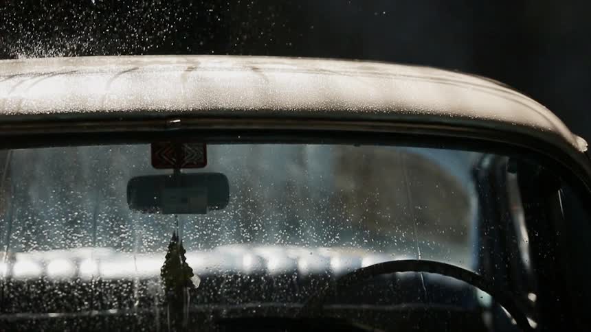 Rain falls on an old car at night