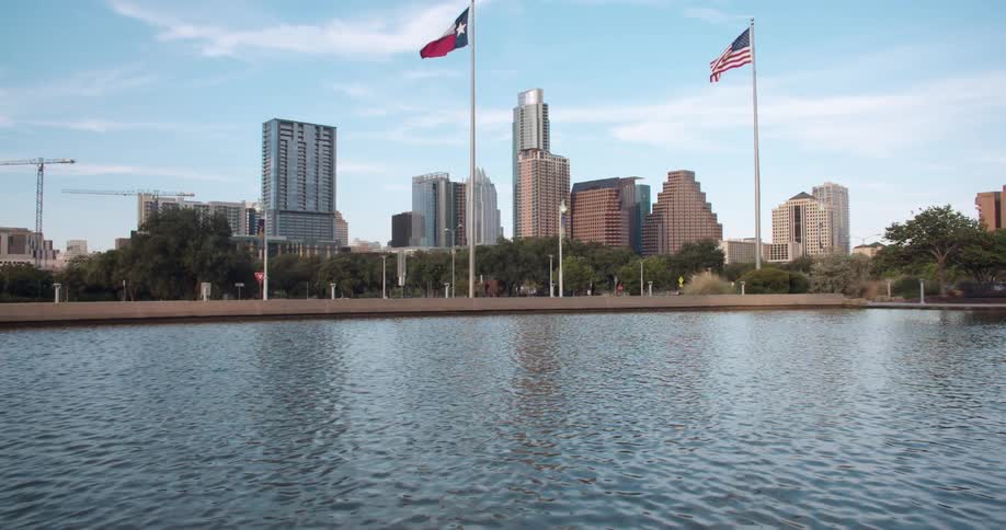 View of two flag poles with flags blowing in the wind before a city