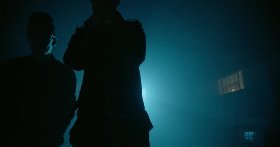 Two rappers dance around in a dark room