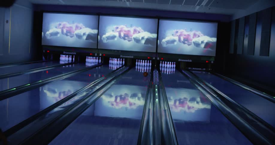 A man rolls a bowling ball down a lane