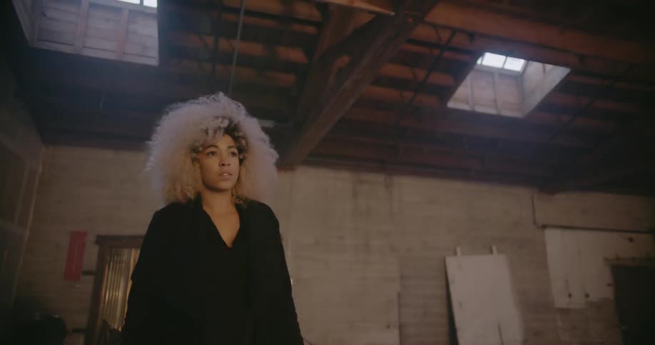A woman is walking towards a glowing light in an empty warehouse during the day